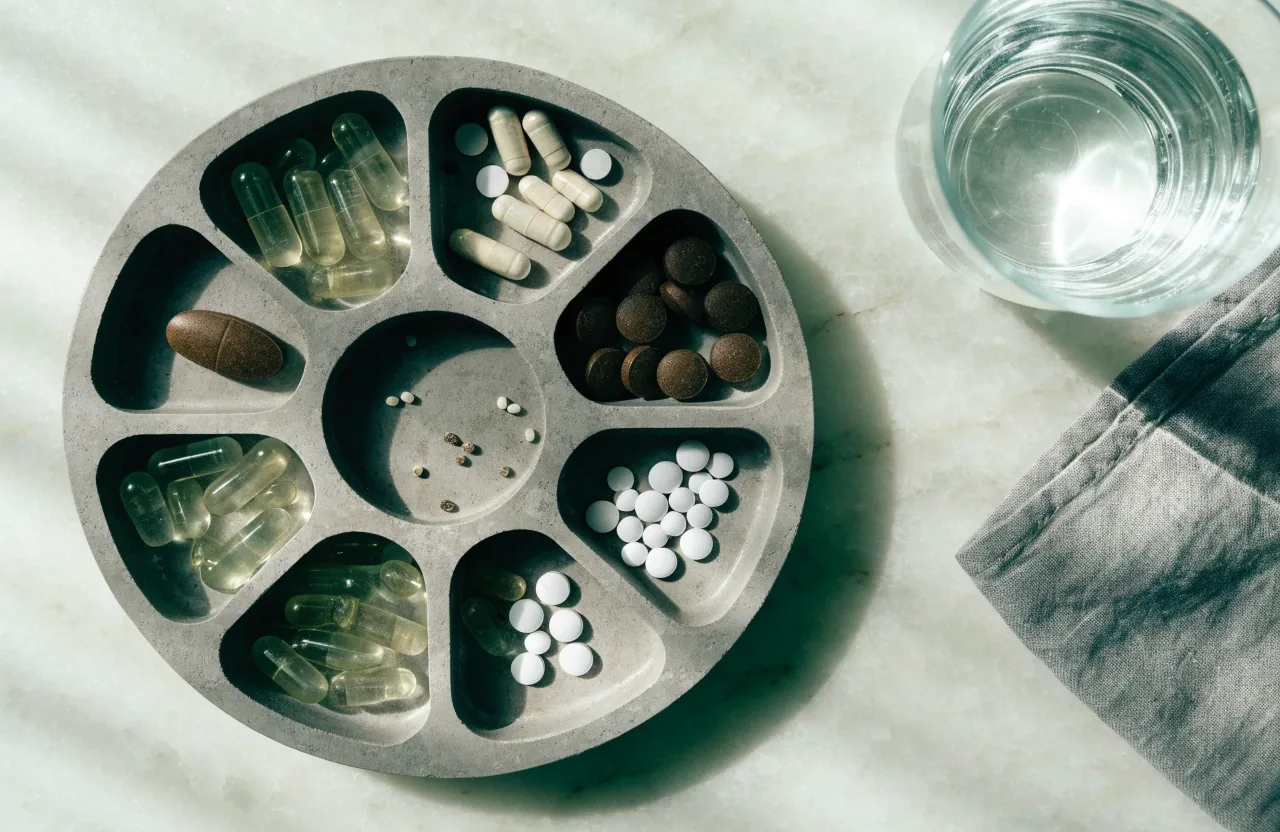 A seven-compartment supplement tray on a pale counter with clear capsules and tablets arranged inside it